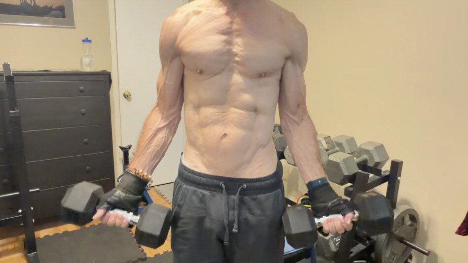 John demonstrating the lowered starting position of a standing dumbbell biceps curl