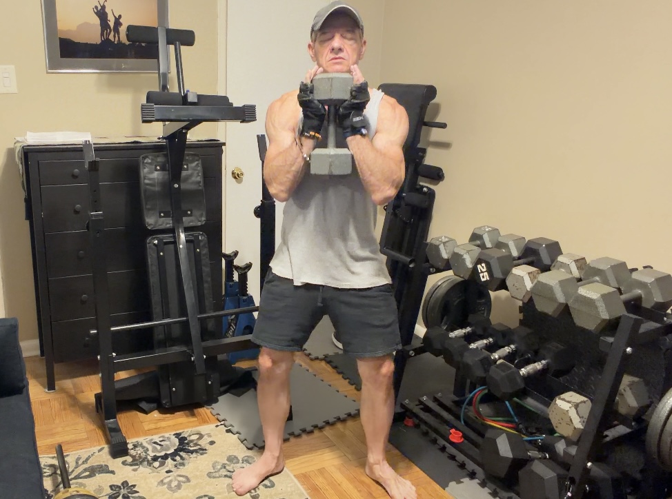 John standing tall with a dumbbell held securely at his chest at the start of a goblet squat