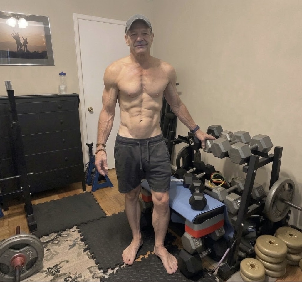 John standing beside the dumbbells and equipment in his compact home workout room