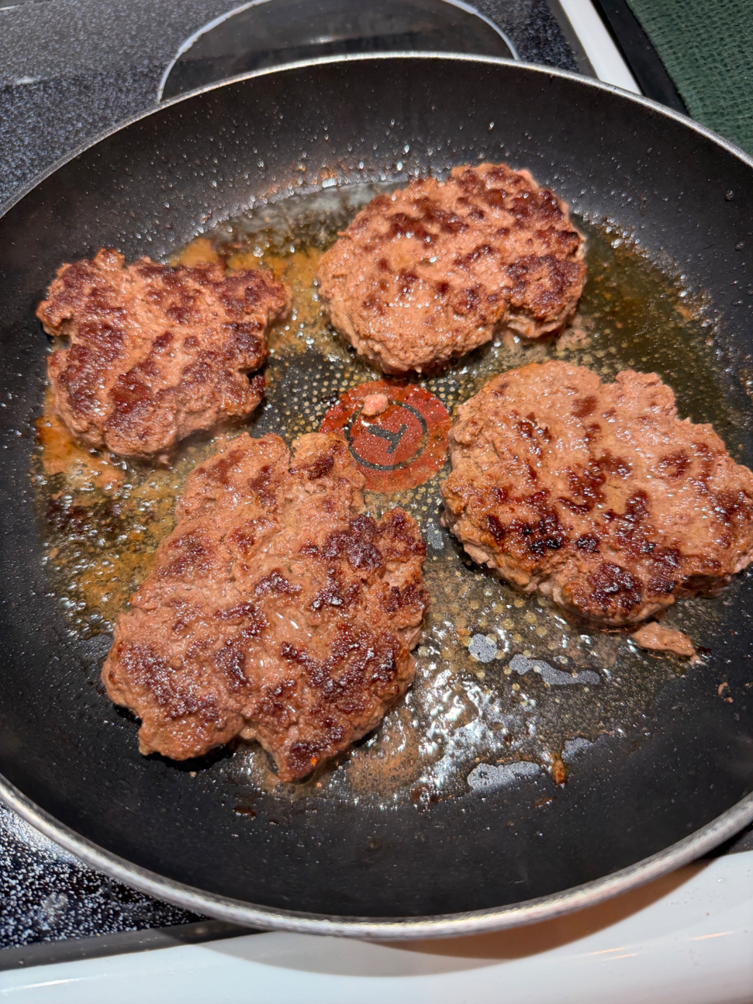 Four browned beef patties cooking in ghee