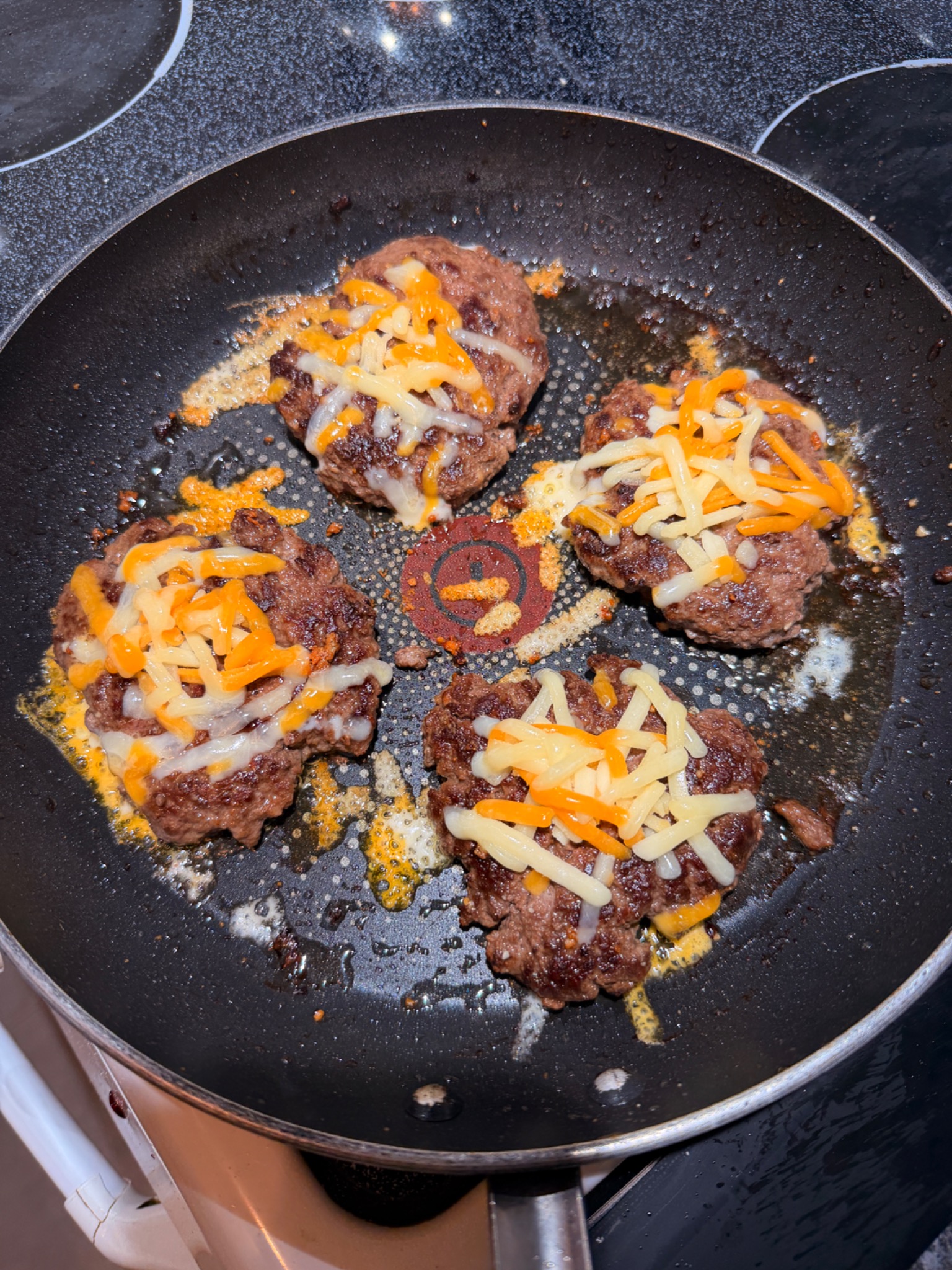 Shredded cheddar melting over browned burger patties