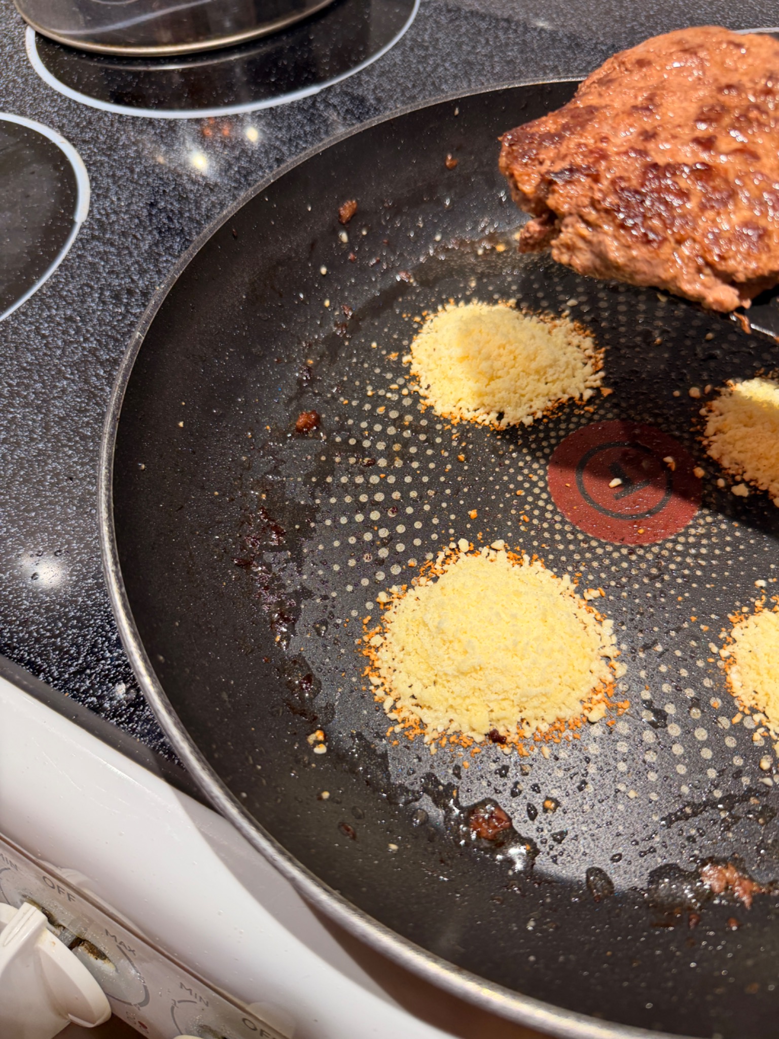 A browned burger being placed over grated Parmesan in the pan