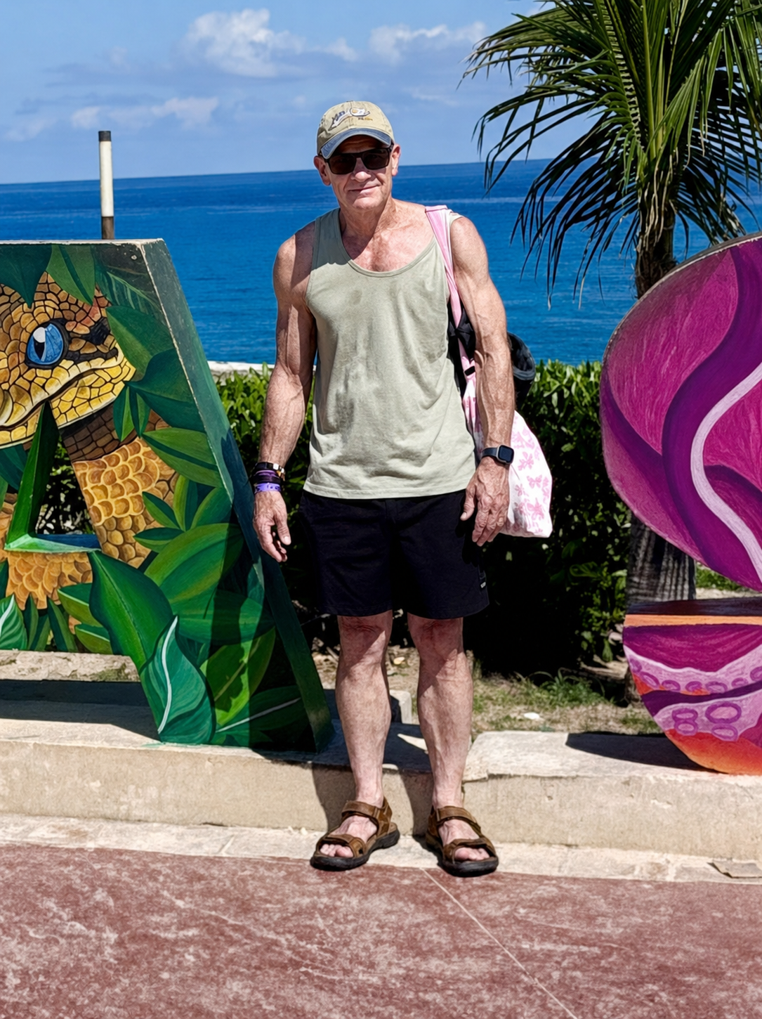 John smiling beside colourful tropical artwork with the ocean behind him